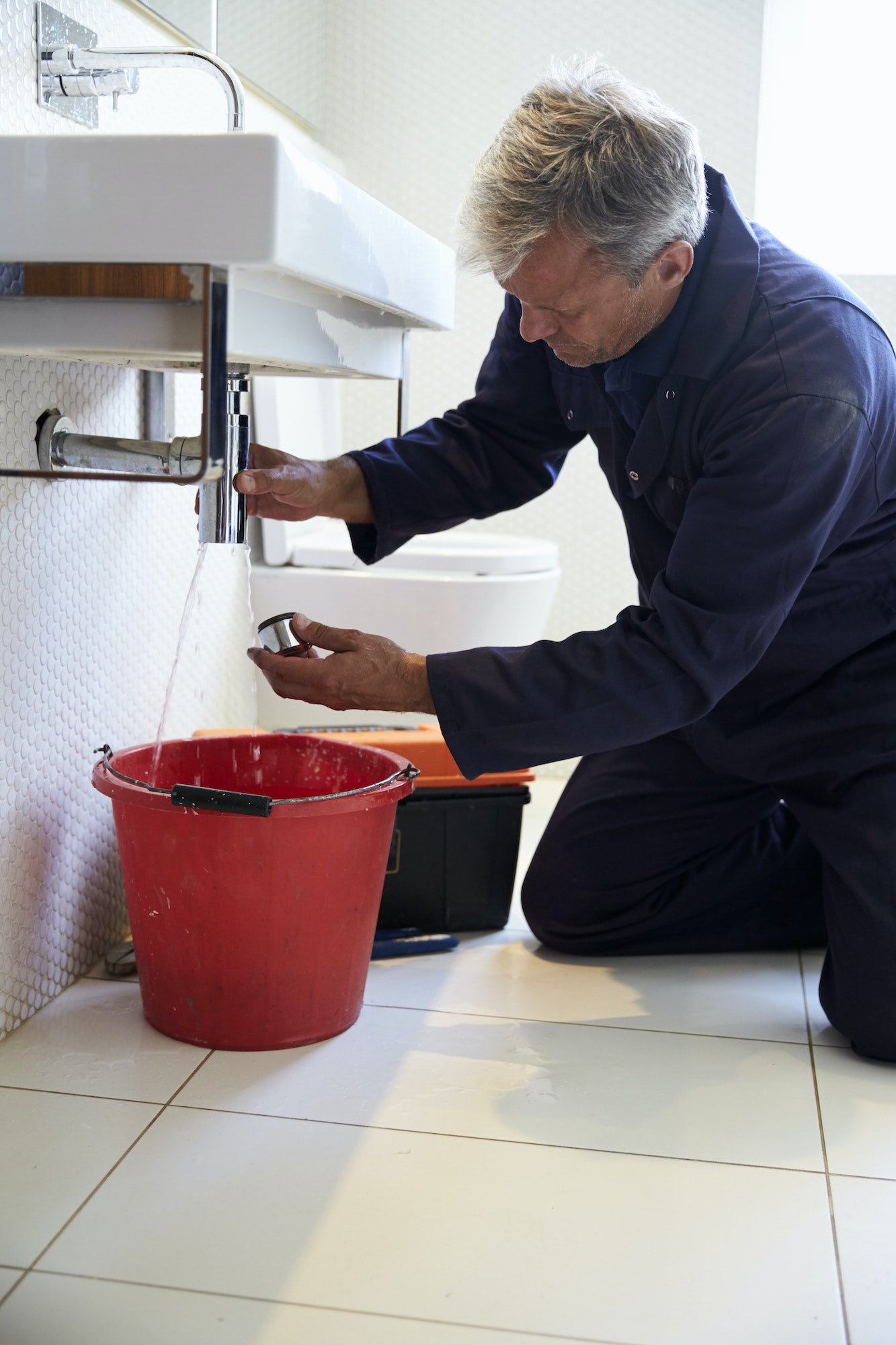 Plumber Working On Sink In Bathroom
